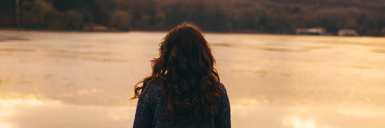 Mental Illness: I Don't Know How I Feel Most Days Woman wearing a jacket, standing in front of lake at sunset