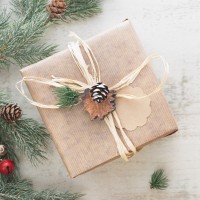 christmas gift wrapped in light brown paper next to christmas tree branches and acorns