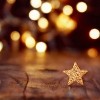 Holiday lights in background with gold glittering star on wood table