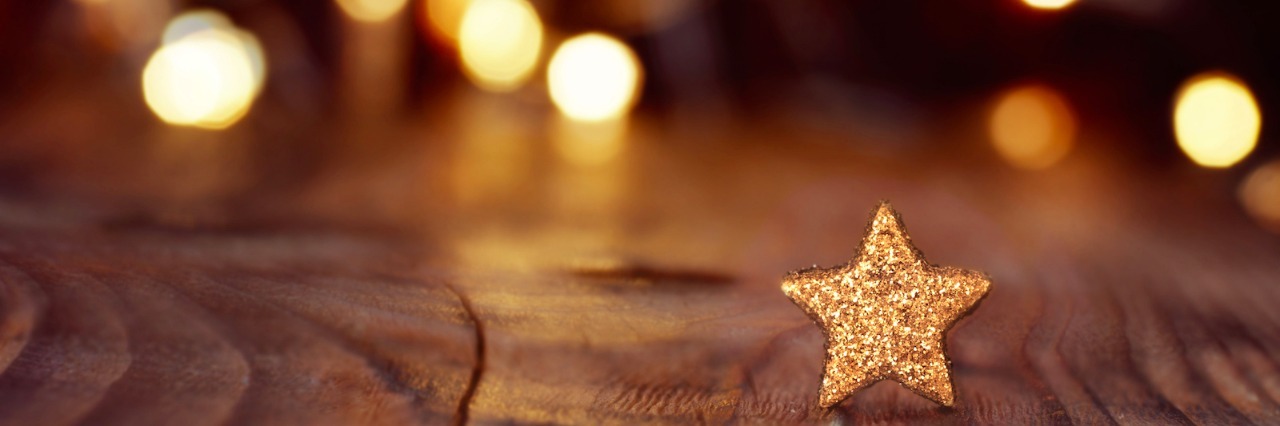 Holiday lights in background with gold glittering star on wood table