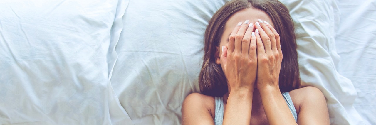 a girl laying in bed covering her face with her hands