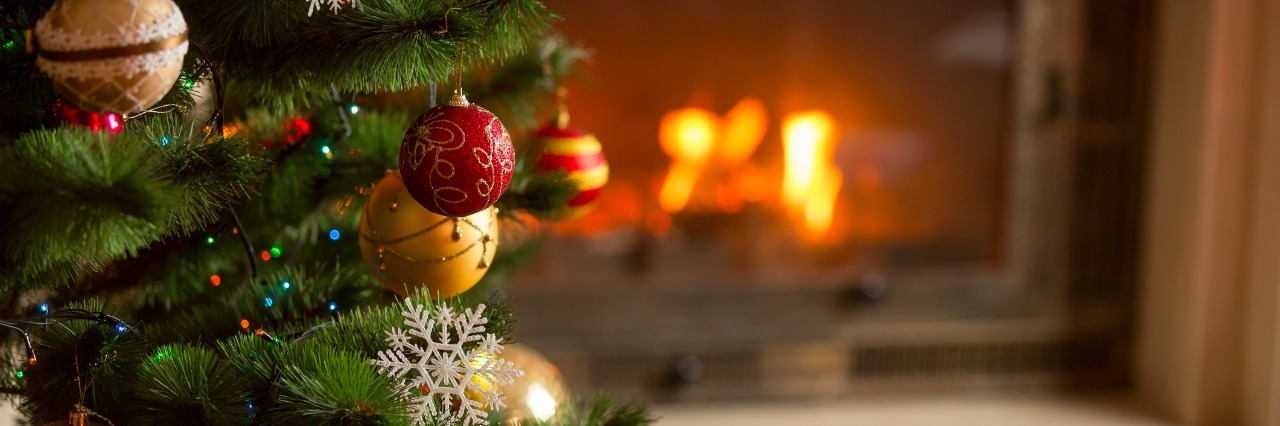 closeup image of golden baubles on Christmas tree at fireplace
