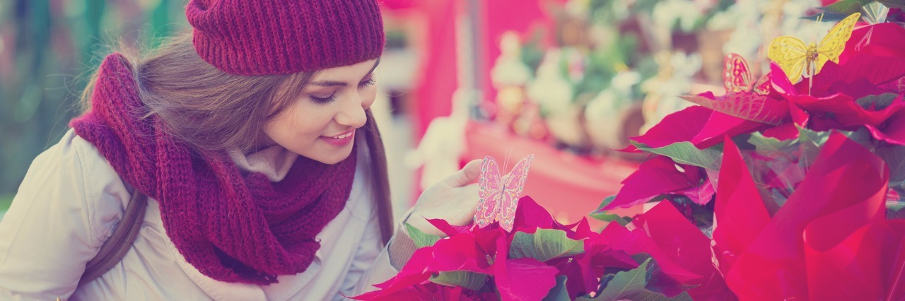 woman in red scarf and hat looking at poinsettias outside at a christmas market