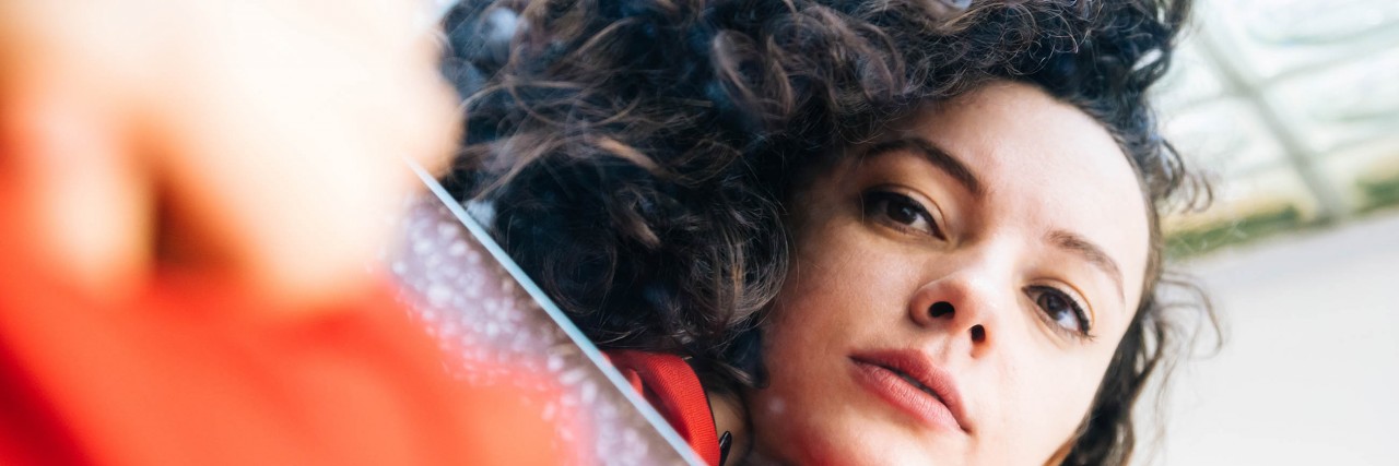 The Invisible Tattoos of Bipolar Brunette woman with curly hair looking in mirror and seeing her reflection