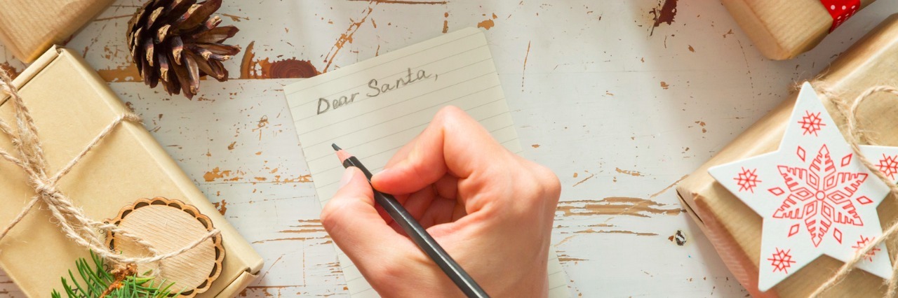A Christmas List to Santa From an Autistic Adult and Therapist Person writing a letter to Santa on a wood table with wrapped presents on it