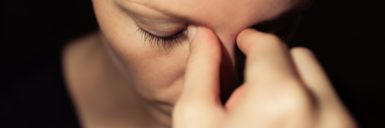 woman pinching the bridge of her nose and looking tired and stressed