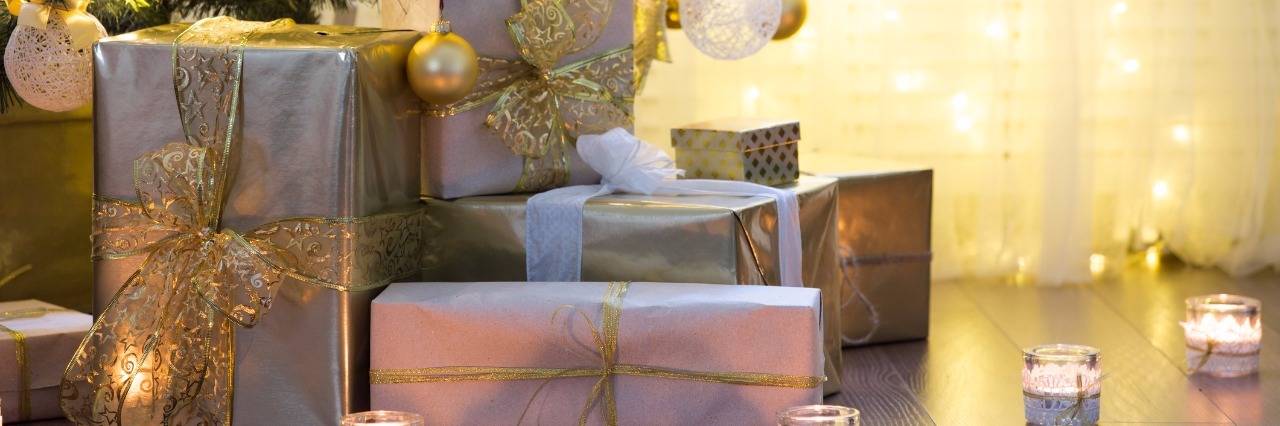 10 Gift Ideas For Those With an Invisible Mental or Physical Illness Tall christmas tree, beautifully decorated with balls, bows and lights. Lots of christmas gifts under the tree. Candles on wooden floor.