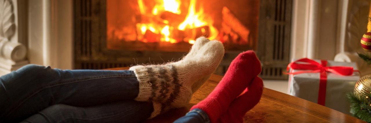 Making Christmas Day Plans With Chronic Back Pain a couple wearing festive woolen socks relaxes in front of the fireplace and their christmas stockings