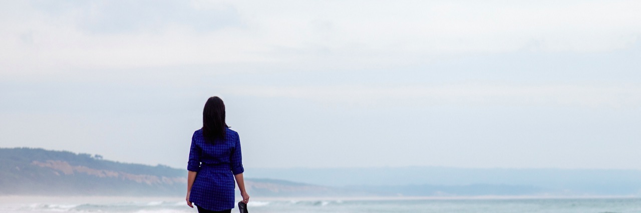 Fear of Letting Go of Grief After My Mom's Passing Woman holding shoes while walking on beach on an overcast day