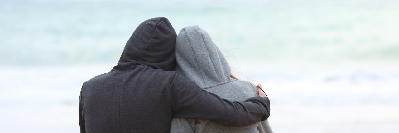 Accepting Not Everyone Will Get My Life With Chronic Illness Two people wearing hoodies, hugging while facing the ocean on the beach