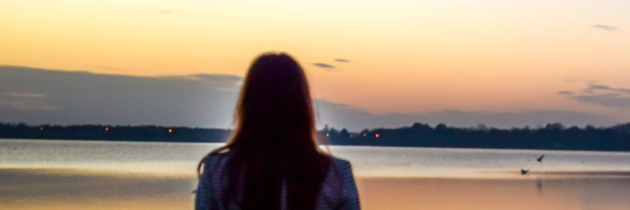 Woman facing lake at sunset