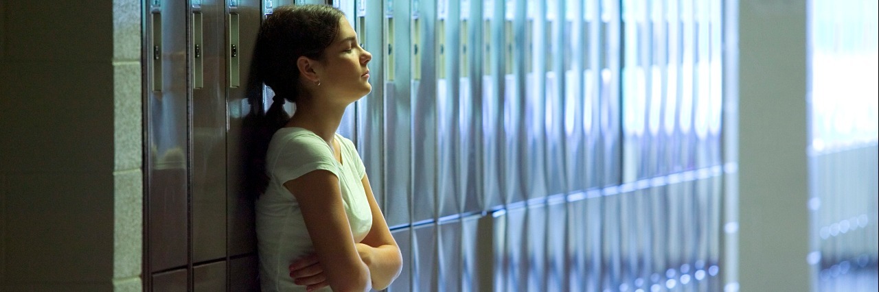 teenage girl leaning against lockers with her arms crossed at high school