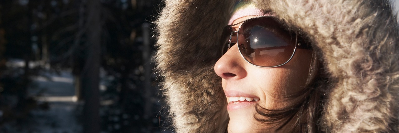 How Chronic Migraines Affect Clothing Choices woman wearing heavy coat with fur hood and sunglasses and standing outside in the snow