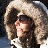 woman wearing heavy coat with fur hood and sunglasses and standing outside in the snow