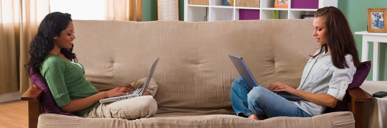 Two women sitting on opposite sides of the couch, using laptops