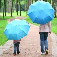 mother and child holding umbrellas, walking on a path in the park