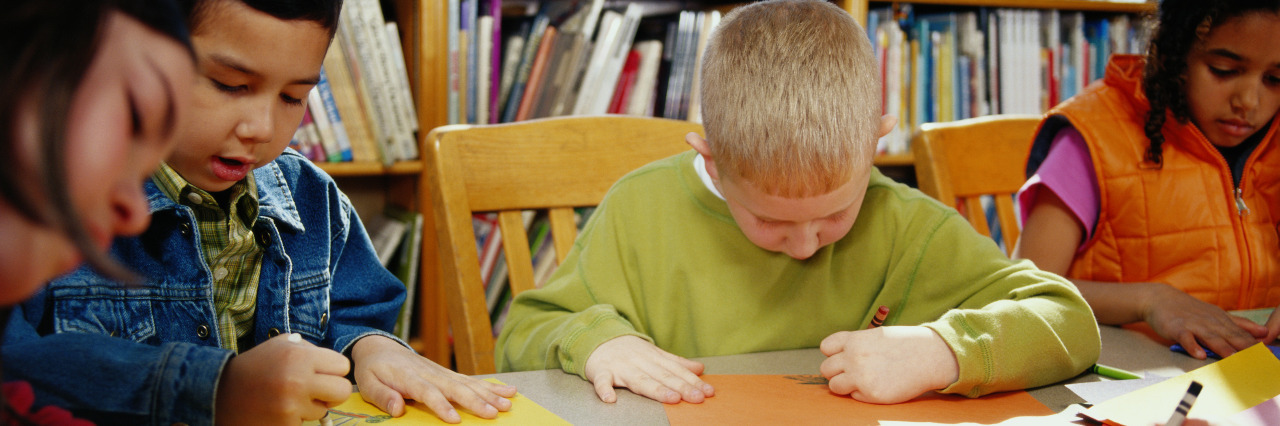 Children coloring with crayons at table in classroom.