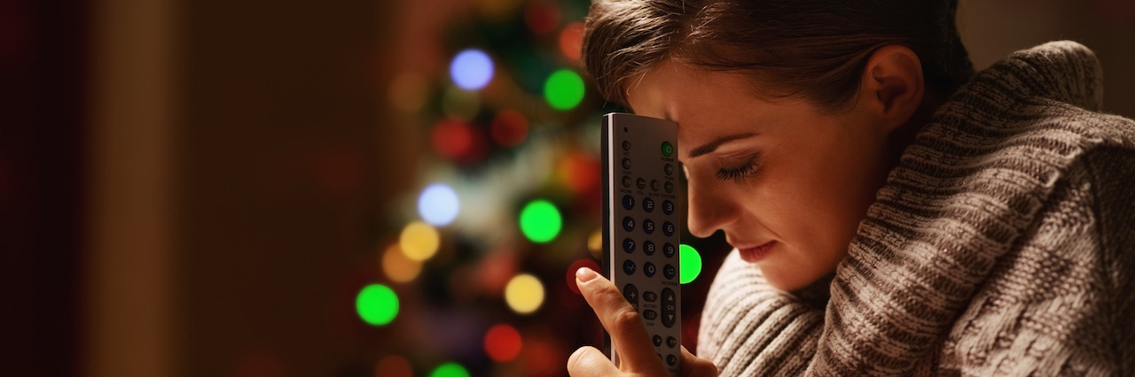 5 Things My Depression Prompted Me Let Go of This Holiday Season Frustrated young woman with tv remote control in front of christmas tree