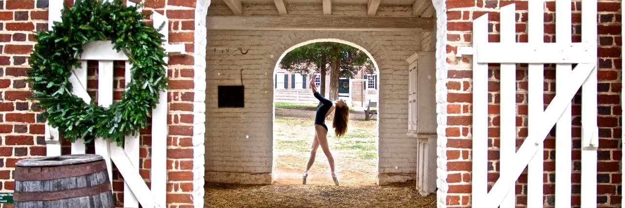 woman in ballet pose under doorway of brick building