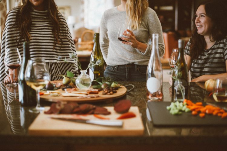friends sitting and standing around a table with food and wine on it