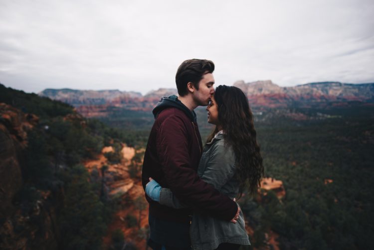 man and woman standing on mountain with the man kissing the woman