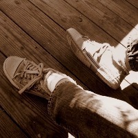 a person's feet wearing old sneakers against a wooden floor with sunlight hitting the feet