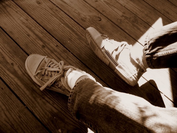 a person's feet wearing old sneakers against a wooden floor with sunlight hitting the feet