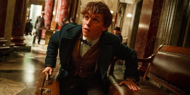 A screenshot from "Fantastic Beasts," a man holding a briefcase crouches and looks up