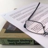a pair of glasses lying on an essay and a textbook