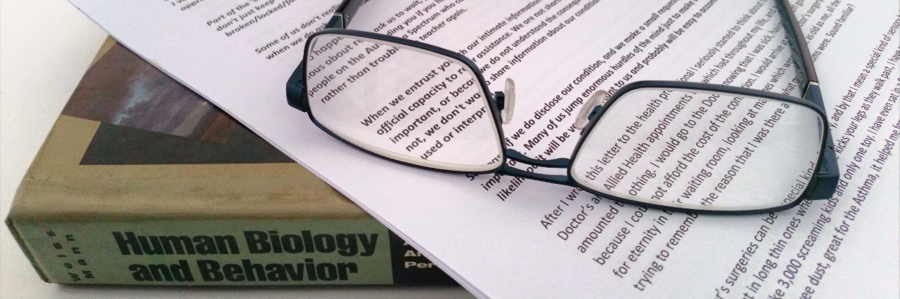 a pair of glasses lying on an essay and a textbook