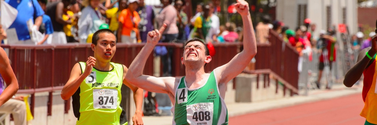 Runner running to the finish line with his hands triumphantly raised.