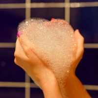 woman's hands holding bubble bath foam in the shape of a heart
