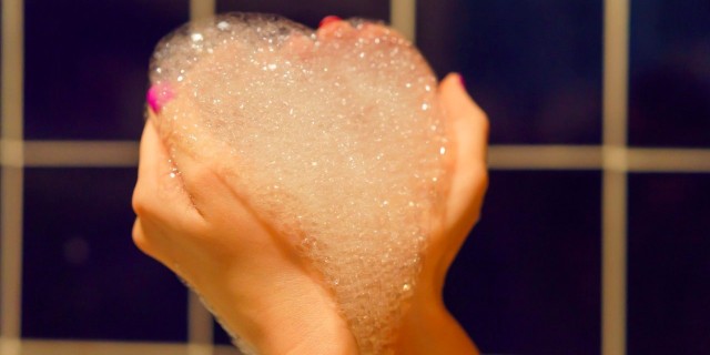 woman's hands holding bubble bath foam in the shape of a heart