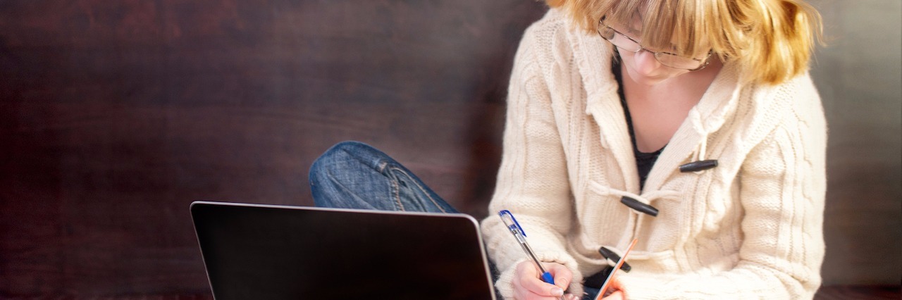 When a College RA Made Me Feel Less Alone in My Depression girl student preparing for exams in bed. On the bed of the book and a laptop. She writes in a notebook.