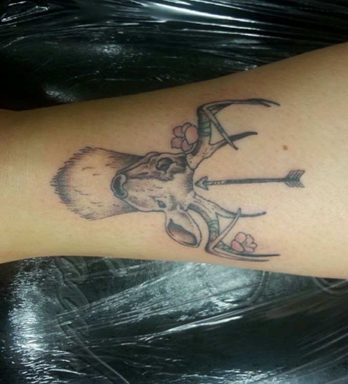 A tattoo of a deer, an arrow and flowers around its antlers