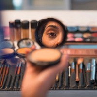 woman looking in compact mirror before putting on makeup