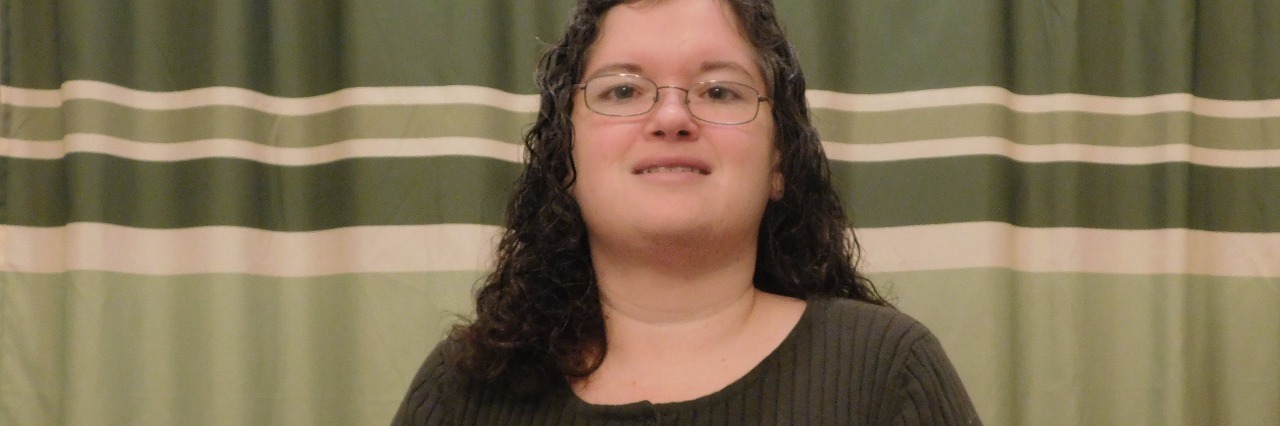 Gastroparesis, Complex Regional Pain Syndrome: What Illness Looks Like woman in dark shirt and glasses smiling in front of striped green curtain
