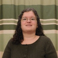 woman in dark shirt and glasses smiling in front of striped green curtain