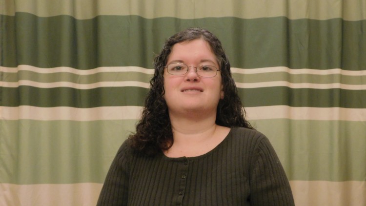 woman in dark shirt and glasses smiling in front of striped green curtain