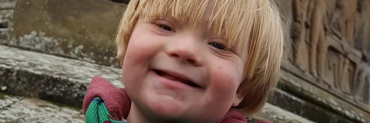 Letter to My Little Brother With Down Syndrome, Who Changed My Life Rory, a little boy with Down syndrome who is wearing a maroon winter coat and green striped scarf.