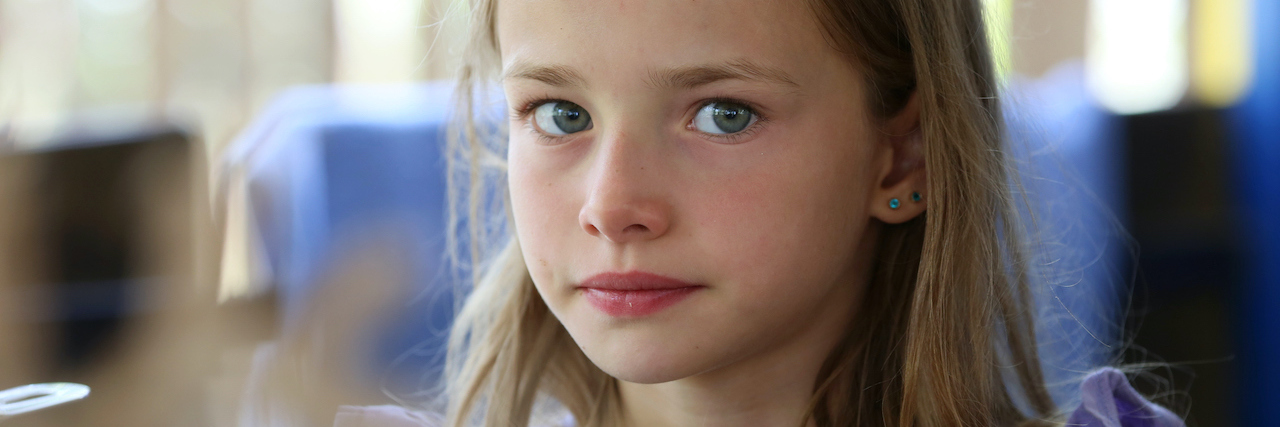 Portrait of a little girl with long hair and blue eyes of a blonde who is resting in nature,