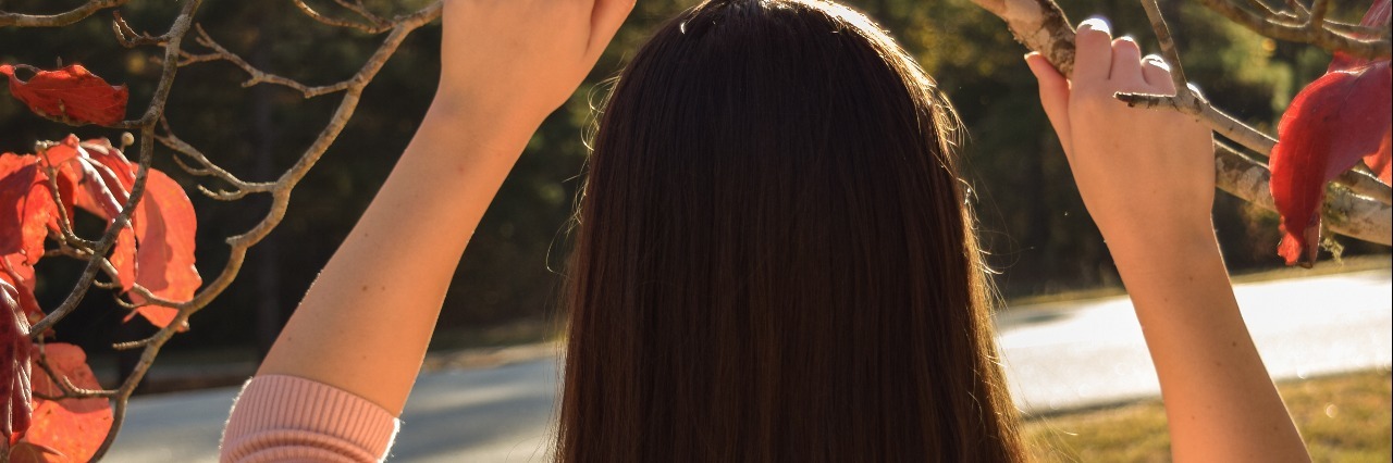 Lyme Disease: Staying Positive and Loving Yourself woman with long brown hair standing outside under a branch with autumn leaves