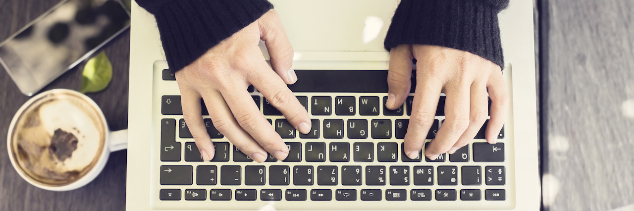 Woman typing on a laptop, with cell phone and coffee