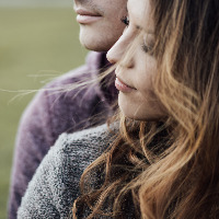 Young loving couple outdoors sitting on grass, hugging and looking away, future and relationships concept