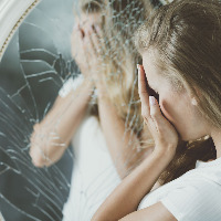 Woman with mental problems covering her face reflected in mirror