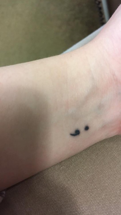A semi-colon tattoo on a man's wrist