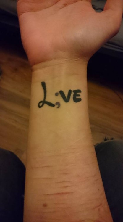 A woman shows off her forearm with the word "Love" with the "o" replaced by a semicolon