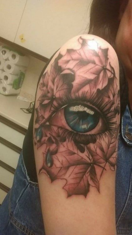 A tattoo of an eye on leaves on a shoulder