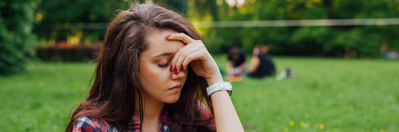 Why You Shouldn't Joke About OCD A young woman sitting on the grass looking annoyed
