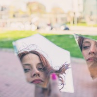 Beautiful redhead girl with long hair and blue eyes looking at herself in a broken mirrorBeautiful redhead girl with long hair and blue eyes looking at her reflection in a broken mirror